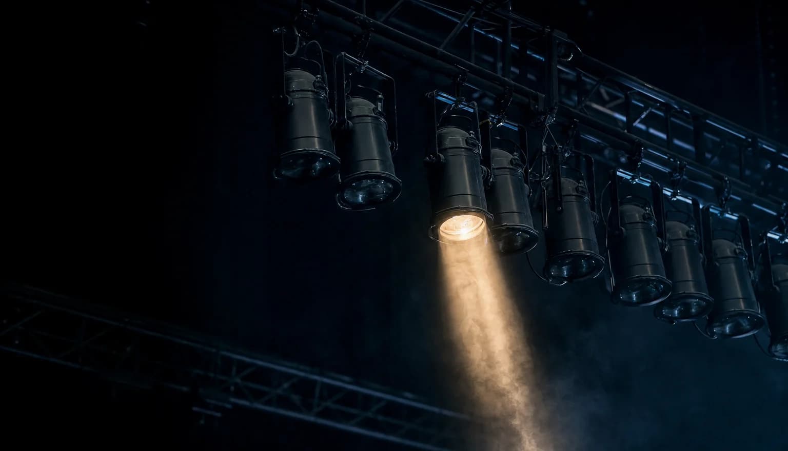 A grid of stage lamps in a dark rig, most dark and one relighting